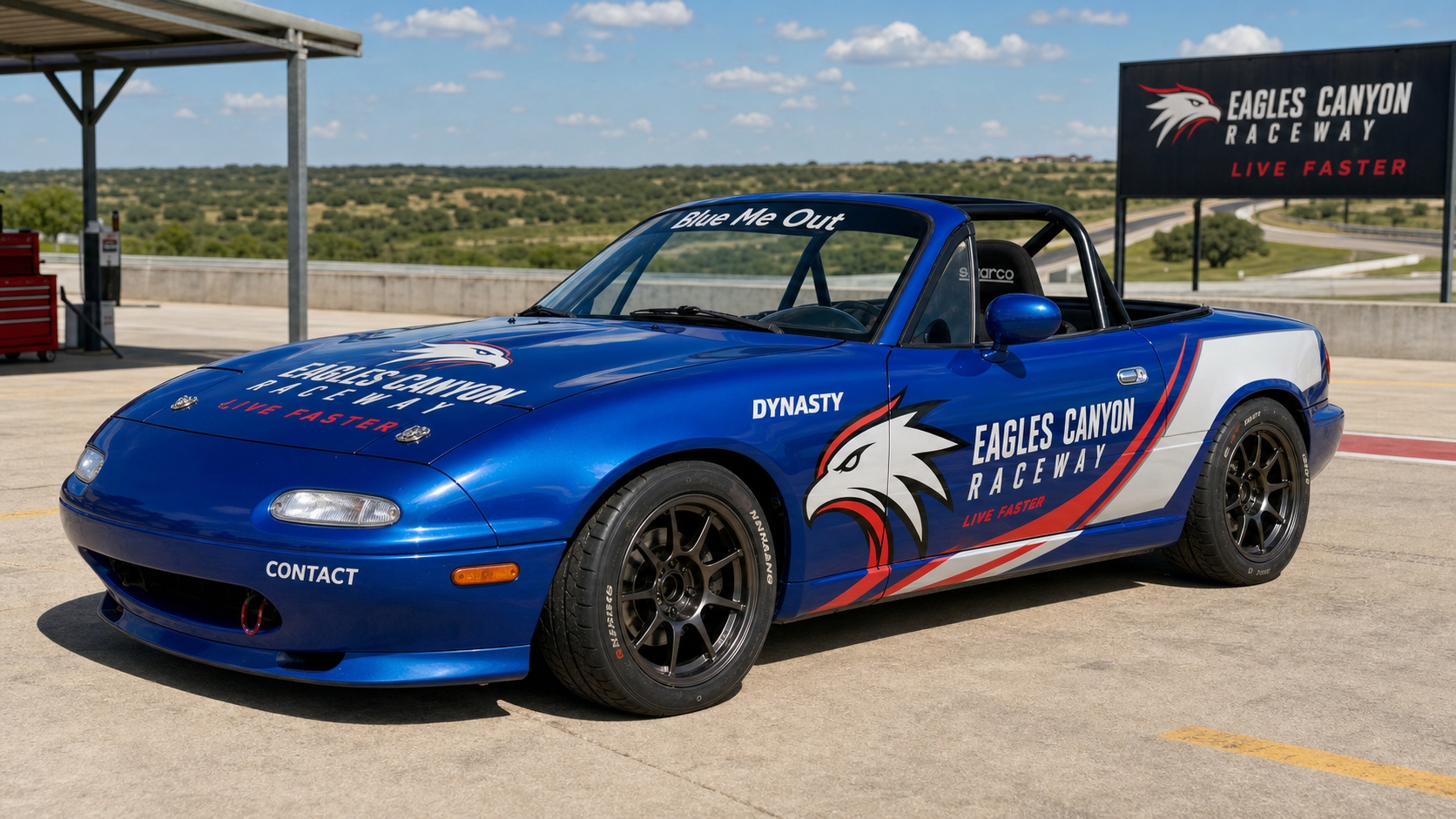 1991 Mazda Miata in Mariner Blue with official Eagles Canyon Raceway livery — Live Faster wrap, Dynasty door graphic, Blue Me Out windshield banner, black wheels, in the paddock at Eagles Canyon