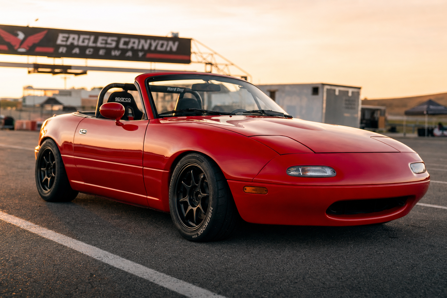 1991 Miata Track-Ready build in Ferrari Race Red · your color, your canvas · coilovers, BBK brakes, black wheels on Hankook RS4 semi-slicks, Hard Dog roll bar, Sparco seat · Eagles Canyon paddock at golden hour